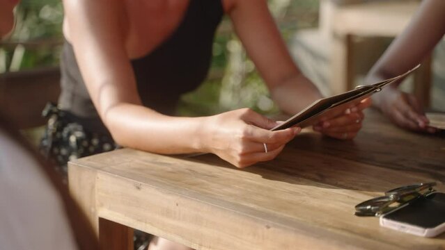 Woman reads restaurant menu in tropical restaurant close-up. Female hands holding menu in seaside outdoor cafe turns pages, chooses food and drinks. Pick refreshers and beverages. Select appetizers