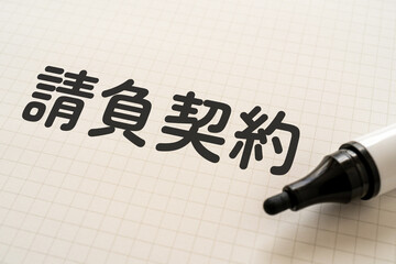 請負契約と書かれたノートとマーカー