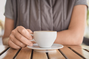 Close-up of a cup of cappuccino or hot drink and the hands of a young woman drinking coffee during a break. Selective focus on fingers, idea for background