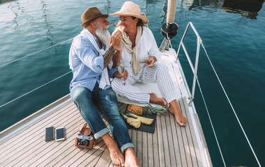 Senior couple drinking champagne on sailboat during summer vacation - Soft focus on woman hat