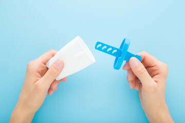 Young woman hands holding opened white plastic container for homemade ice popsicle on stick. Light blue table background. Pastel color. Closeup. Cold sweet snack. Point of view shot. Top down view.