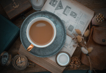 Hot coffee in ceramic cup and brass coffee spoon served with Fresh milk on worktable with old book,...