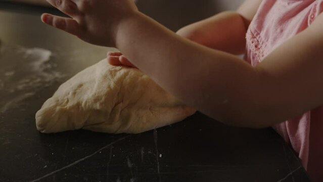Baby girl's hands kneading dough for home baking bread on a kitchen table. Small hands, cooking concept, childhood.