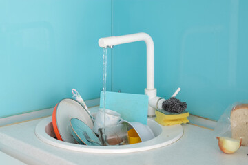 A sink full of dirty dishes in the kitchen. Water from an open tap flows into the sink.