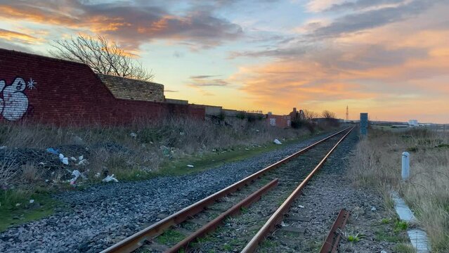 Panning shot of a train track or railroad at sunset, next to graffiti on a wall and litter on the ground.