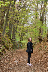 A girl walking a small dog in the forest in the early spring