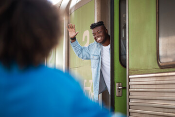 Cheerful Black Man Waving Hand To Girlfriend While Standing In Train Door