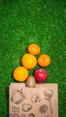 Banana, red apple and different fruits with craft paper bag laying on grass, flat lay. Space for text. Zero waste concept.