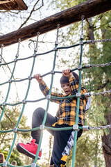 Toddler boy climbs up a high alpine grid on wooden playground in public adventure park. Children outdoor equipment for entertaining and recreation, healthy lifestyle and muscle development