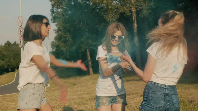 Three happy beautiful women making party at Holi colours festival in summer time. Young smiling female friends having fun after music event at sunset. Positive models in sunglasses at sunset