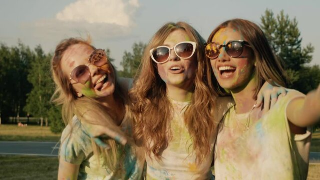 Three happy beautiful women making party at Holi colours festival in summer time. Young smiling female friends having fun after music event at sunset. Positive models in sunglasses at sunset