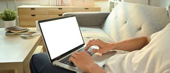 Close up view of man I casual clothes sitting on couch working remotely, surfing internet on laptop
