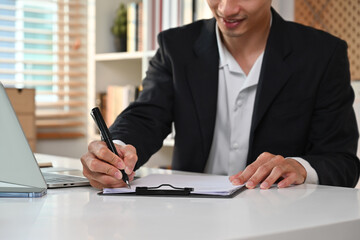 Cropped image of professional businessman in formalwear writing his strategy, signing a contract at working desk