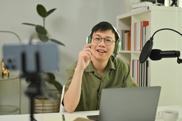 Young man radio host using microphone and laptop to recording podcast in home studio. Radio,...