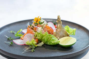 Spicy Raw Salmon Salad Thai food style decorated with Crispy fried fish skin and Yellow Flower on top and micro herb around dish on white background.