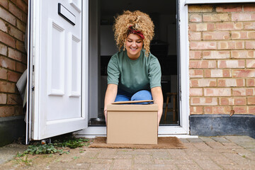 Happy young woman picking up packages from doorway