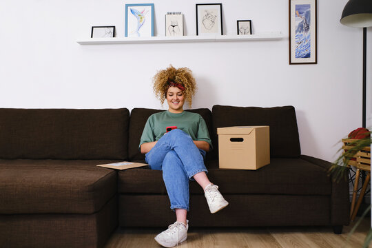 Smiling young woman using smart phone on sofa at home