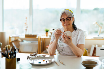 Smiling senior woman painting cup at studio