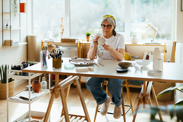 Senior woman painting crockery in workshop