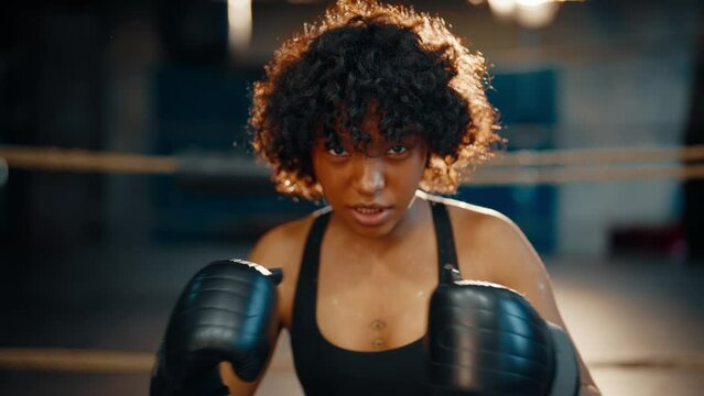Fighter african american curly girl boxer clapping with boxing gloves on boxing ring looks at camera. Sportswoman on training, workout. Sport feminism self-defence and black lives matter concept.