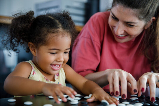 Happy mother and daughter playing go game at home