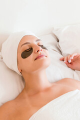 Fototapeta na wymiar Beautiful young woman with under eye patches in bathrobe lying in bed. Happy girl taking care of herself. Beauty skincare and wellness morning concept