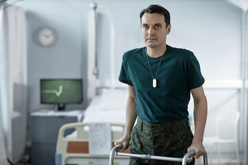 Fototapeta na wymiar Portrait of soldier looking at camera while trying to walk with walker in hospital ward during his rehabilitation