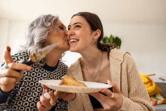 Mother serving cake and kissing daughter at home
