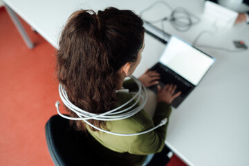 Businesswoman working on laptop tied up in cable at office