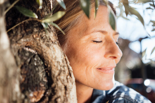 Mature woman with eyes closed embracing tree on sunny day