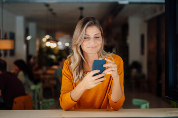 Smiling woman with bond hair using smart phone in cafe