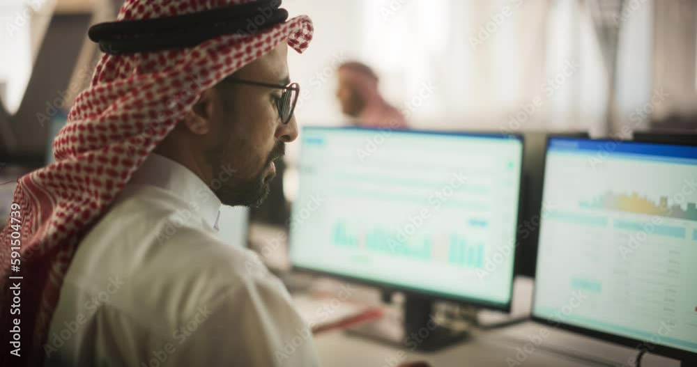 Poster Portrait of a Middle Eastern Financial Securities Trader Working on Desktop Computer in a Modern Office. Arab Bookkeeper Accounting the Financial Affairs of a Business