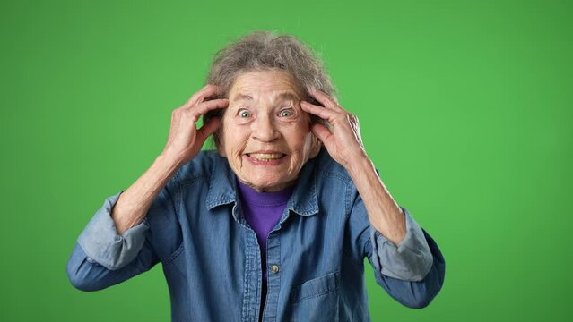 Portrait of elderly senior old woman with wrinkled skin and grey hair looks at camera gives mind blown gesture showing explosion of ideas posing isolated on green screen background with copy space.