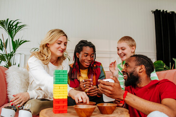 Happy diverse friends playing toy block game and spending leisure time at home