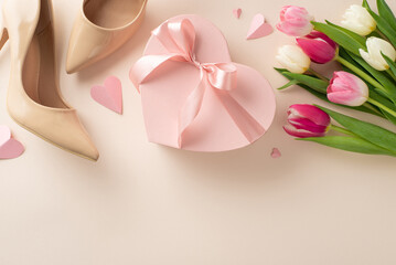 Mother's Day celebration concept. Chic and trendy top view flat lay featuring high-heels, gift box, tulip flowers on a pastel beige background with empty space for text or advert