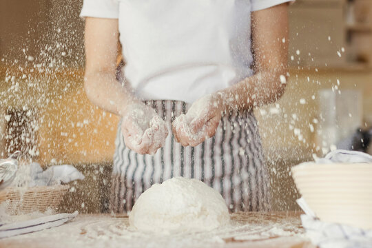 Woman sprinkling flour on dough at home