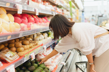Portrait of healthy young Asian woman with casual clothes is wearing medical face mask when buy fresh organic fruit to make healthy food with new normal lifestyle  and social distancing at supermarket