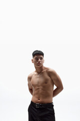 Fototapeta premium Portrait of handsome, muscular young man posing shirtless in pants against white studio background. Vertical image. Concept of male beauty, body and skincare, cosmetology, men's health, sport, fashion