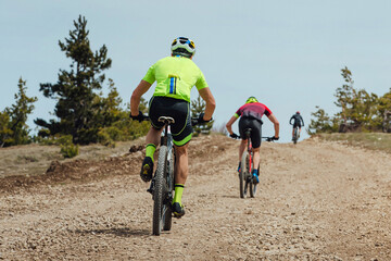 rear view group athlete cyclist riding mountain bike uphill, biking on gravel road, cycling...