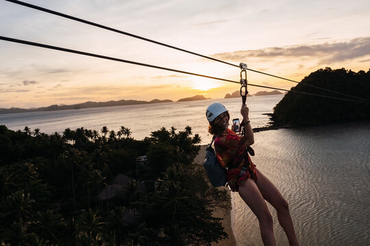 Happy woman enjoying on zip line over beach at sunset