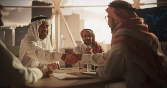 Muslim Businesspeople Closing a Business Deal at a Corporate Modern Office. Two Men in Traditional Clothes Shake Hands and Celebrate Successful Partnership. Saudi, Emirati, Arab Office Concept