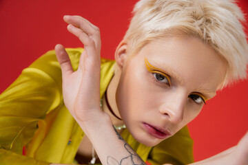 blonde albino woman with bright eyeliner and tattoo looking at camera while posing on carmine pink.