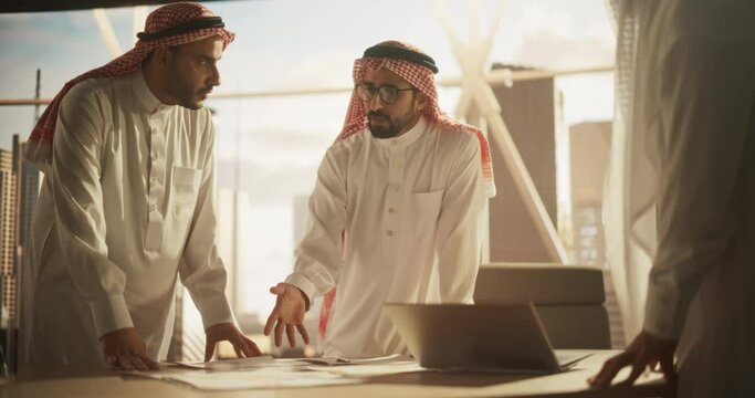 Successful Muslim Businessmen in White Traditional Outfits Having an Office Meeting, Negotiating and Talking About Financial Opportunities. Using Laptop. Saudi, Emirati, Arab Businessman Concept.