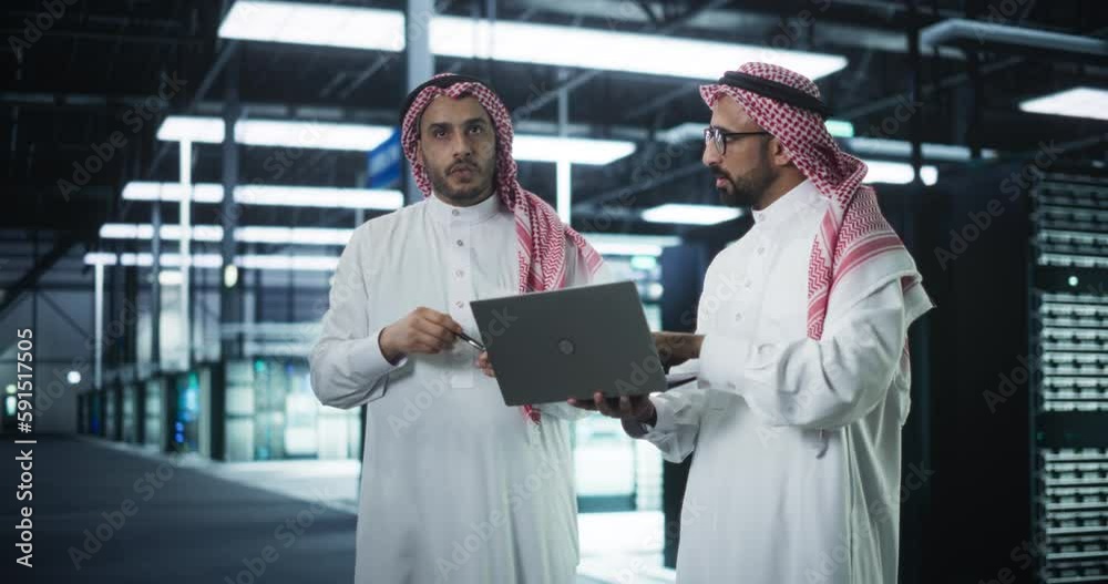 Aufkleber Middle Eastern Computer Engineer and Cybersecurity Professional Work in Server Room, Talk, Perform System Maintenance Check with Laptop Computer. Specialists Doing Database Diagnostics in Data Center