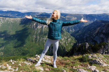 Naklejka premium A young female tourist enjoys climbing the mountains in good sunny weather