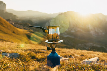 A gas burner with a kettle stands on the rocks overlooking the mountains. Camping kitchen