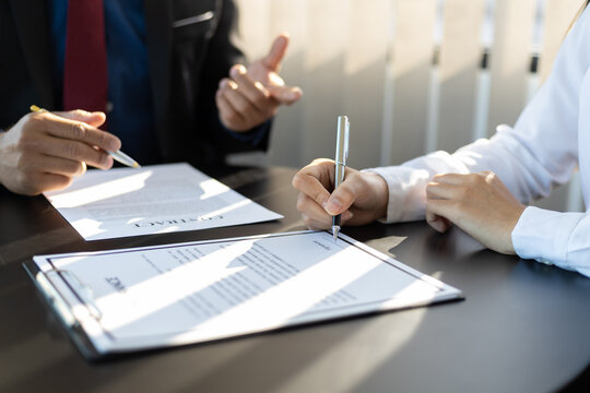 Businessman in suit in his office showing an insurance policy and pointing with a pen where the policyholder must to sign. Insurance agent presentation and consulting insurance detail to customer.