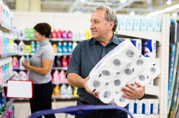 Elderly man chooses toilet paper in supermarket