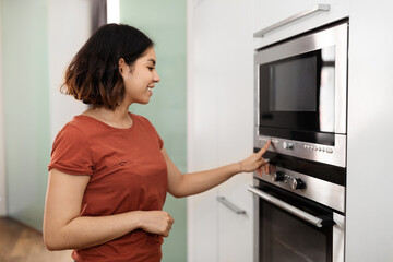 Fototapeta na wymiar Beautiful arab female turning on electric oven in kitchen