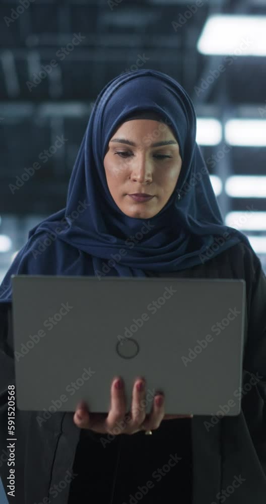 Poster vertical screen: young middle eastern female it system engineer wearing traditional hijab, using lap